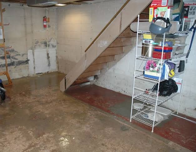 Standing water on concrete foundation floor and damp block walls under basement staircase